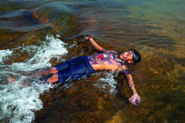 Menino indígena deitado na água corrente de um rio, com o corpo pintado